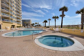 A hotel pool area with multiple swimming pools, palm trees, and a high-rise building in the background.
