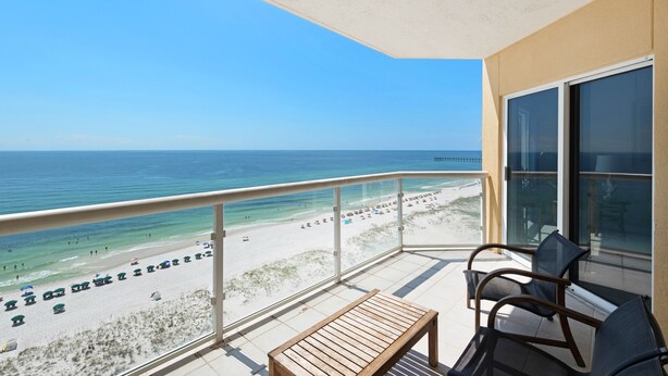 Ein Balkon mit Blick auf Strand und Meer. Auf dem Balkon stehen Stühle und ein Tisch.
