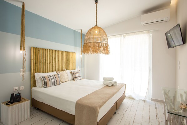 A modern bedroom with a large bed, a hanging light fixture, a bedside telephone, and a television on the wall. - Marini Seaside (Rhodes)