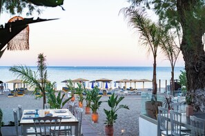 Un restaurante junto a la playa con mesas al aire libre, sombrillas y vistas al mar.