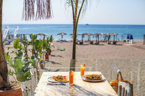 A beachside table with a meal, a drink, and a view of the ocean. - Marini Seaside (Rhodes)