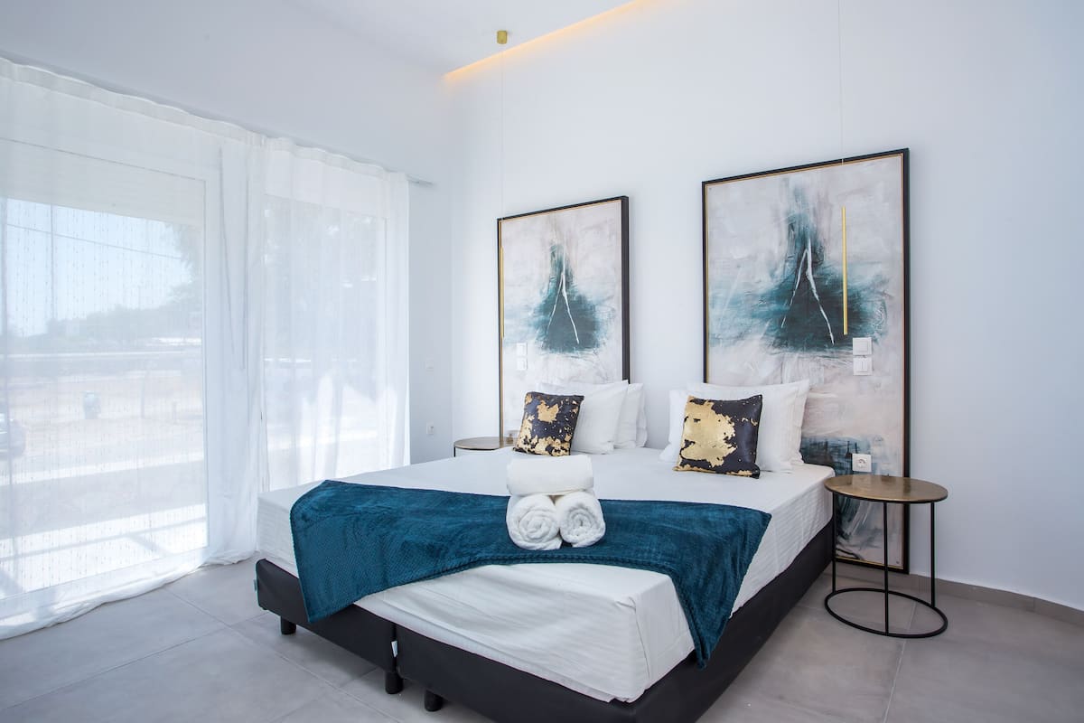 A modern hotel room with a large bed, white linens, a blue throw blanket, and two abstract paintings on the wall.