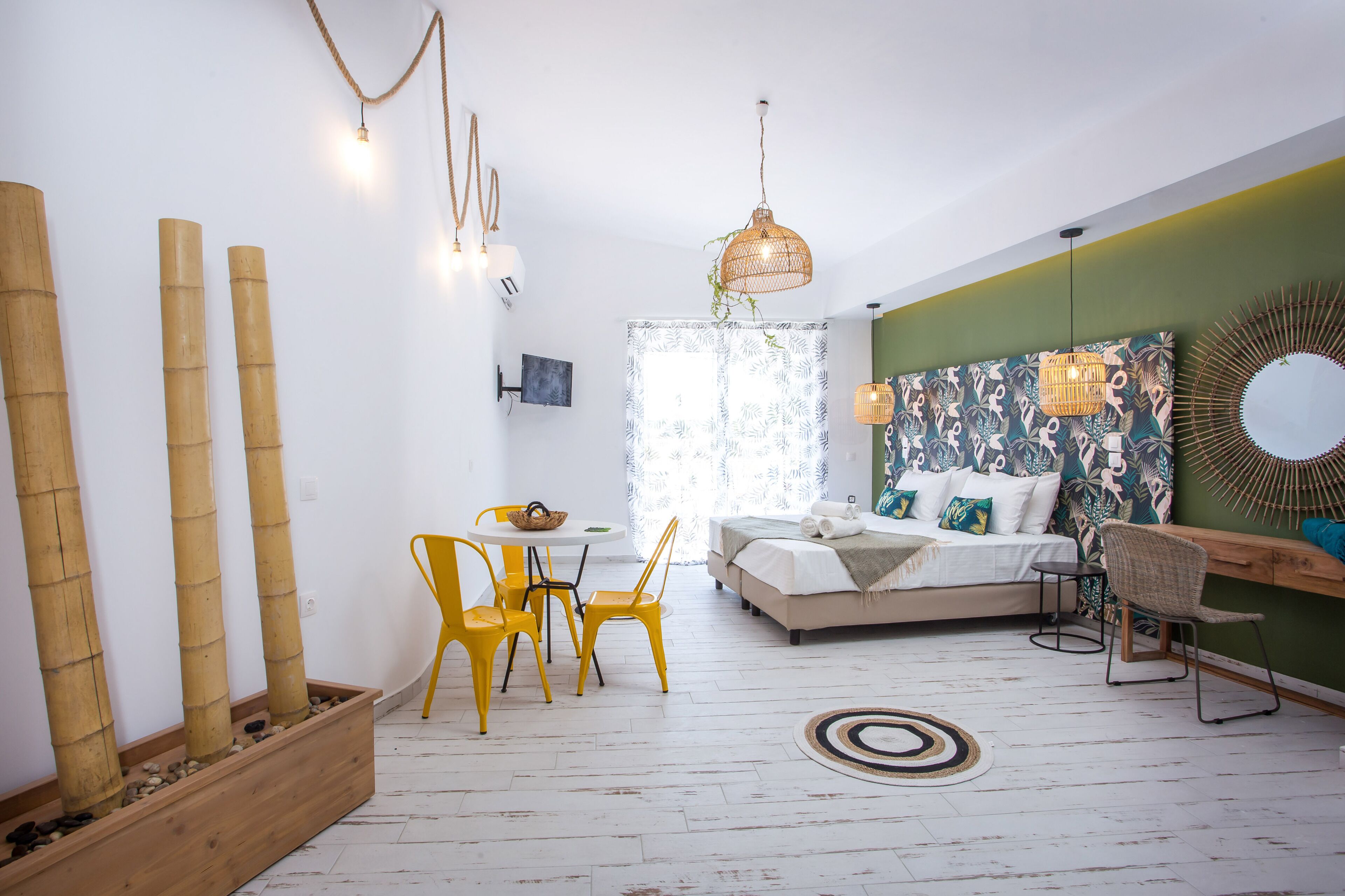 Une chambre à coucher moderne avec un lit, une table de chevet et une chaise. On y trouve une fenêtre avec des rideaux, un téléviseur fixé au mur et un miroir décoratif.