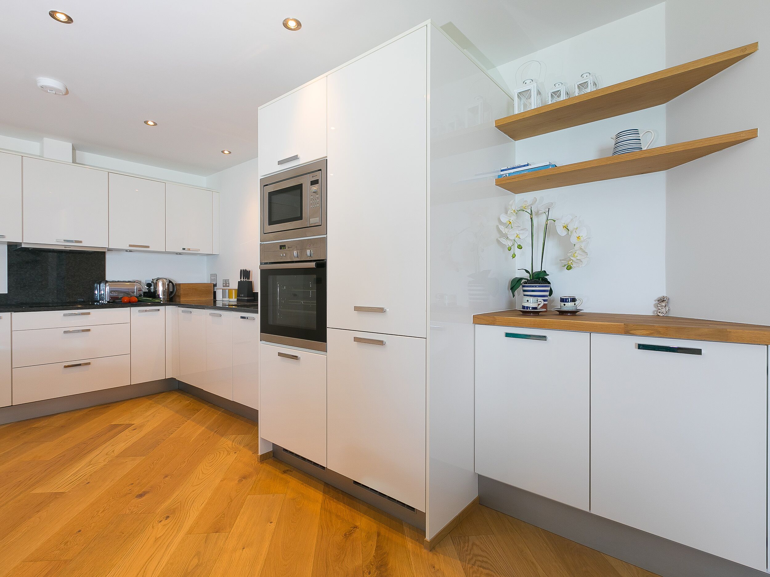 Une cuisine moderne avec des meubles blancs, un four encastré, un four à micro-ondes et un plan de travail en bois.