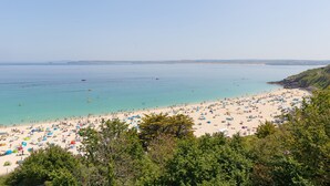 Une plage avec des tentes et des parasols, une eau d’un bleu limpide et un paysage vallonné.