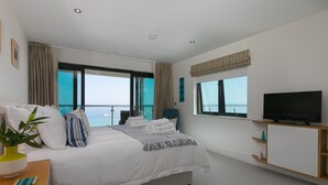 Une chambre d’hôtel moderne dotée d’un grand lit, d’une télévision, d’un balcon avec vue sur la mer et d’un petit bureau agrémenté d’une plante.