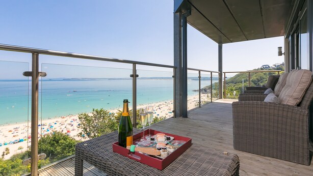 Un balcon agrémenté de meubles en osier, une bouteille de champagne et un plateau de collations, le tout avec vue sur une plage.