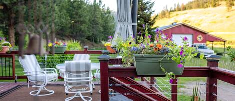 En träveranda med utemöbler, en röd lada och en trädgård med olika växter och blommor.