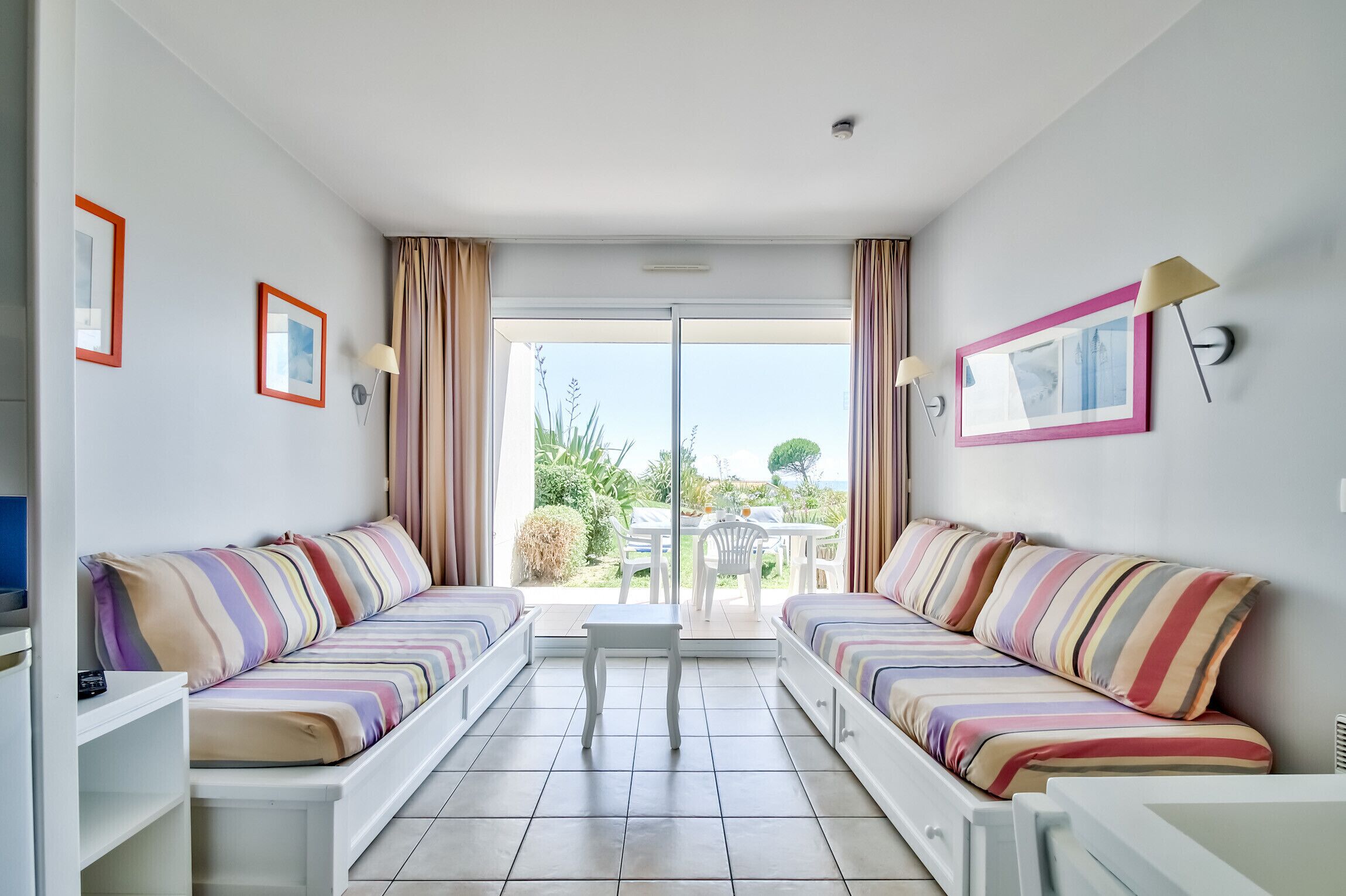 A modern room with two striped sofas, a small table, and a sliding glass door leading to an outdoor area with a table and chairs.