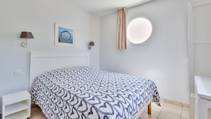 Een slaapkamer met een bed, nachtkastje, lamp, foto aan de muur en een raam met gordijnen.