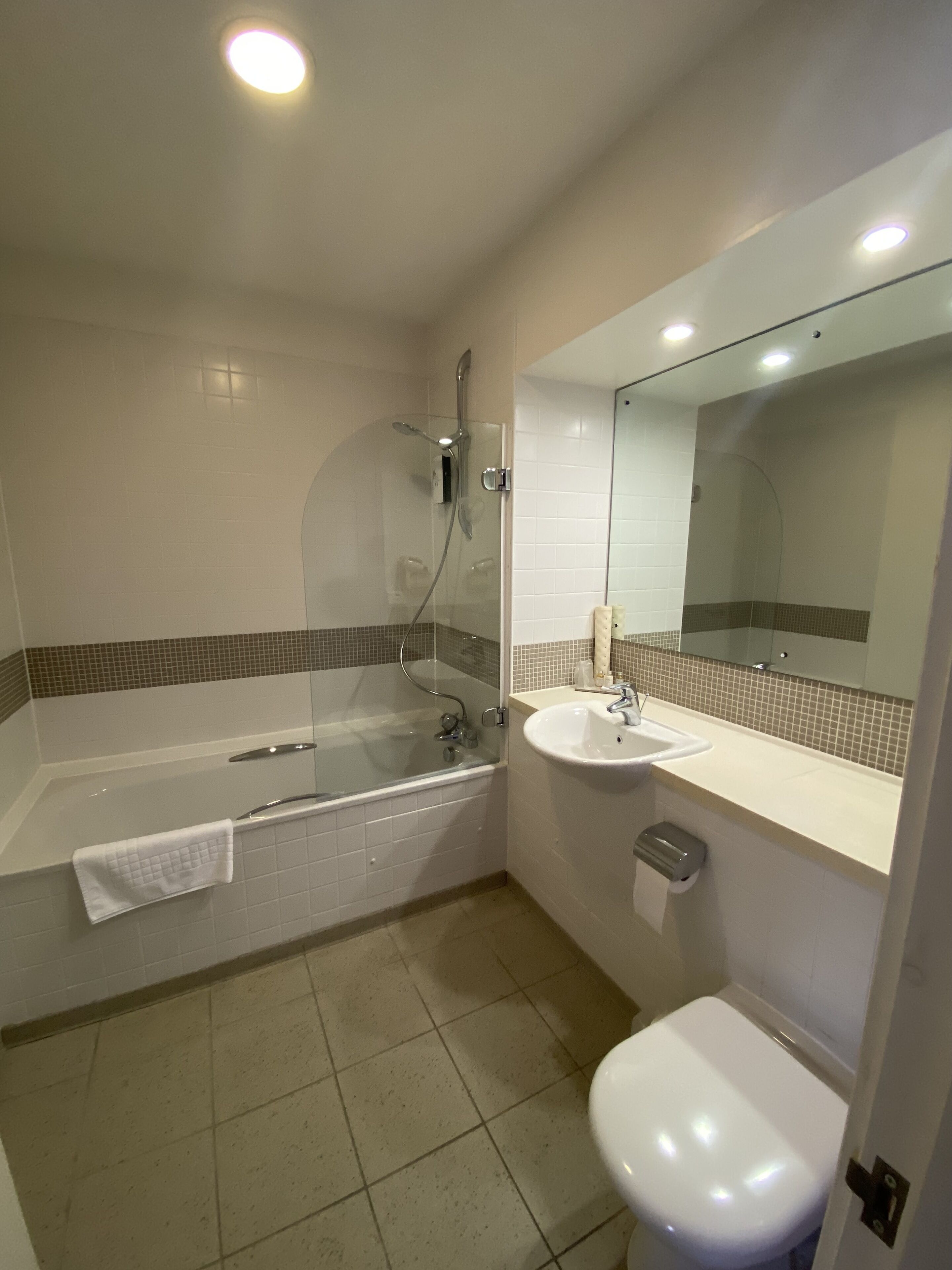 Un baño moderno con ducha de vidrio, bañera blanca, lavamanos y retrete.