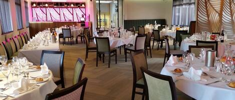 A restaurant with multiple tables set for dining, featuring white tablecloths and neatly arranged cutlery.