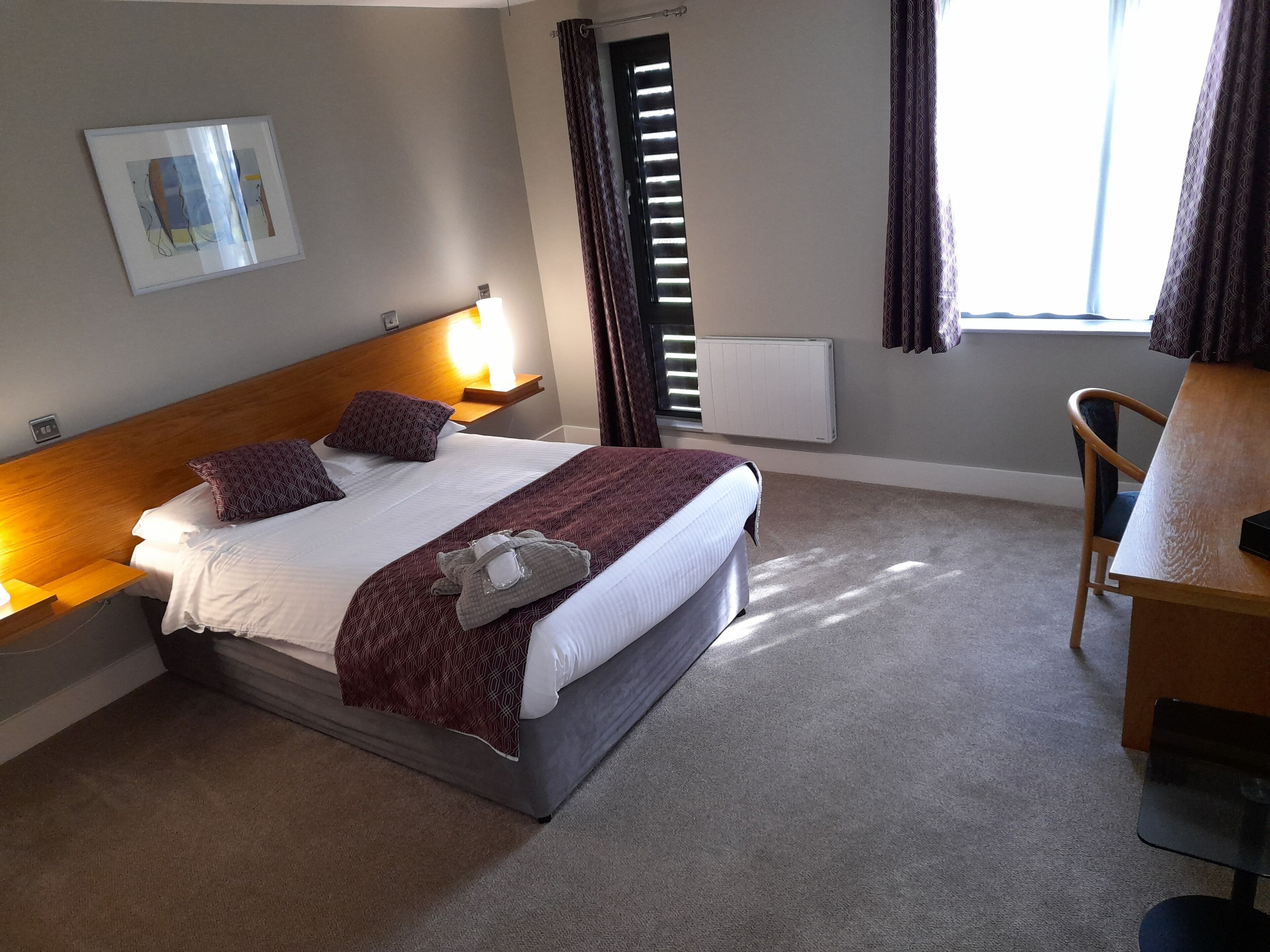 Una habitación de hotel con cama, lámparas de noche, escritorio y una silla.