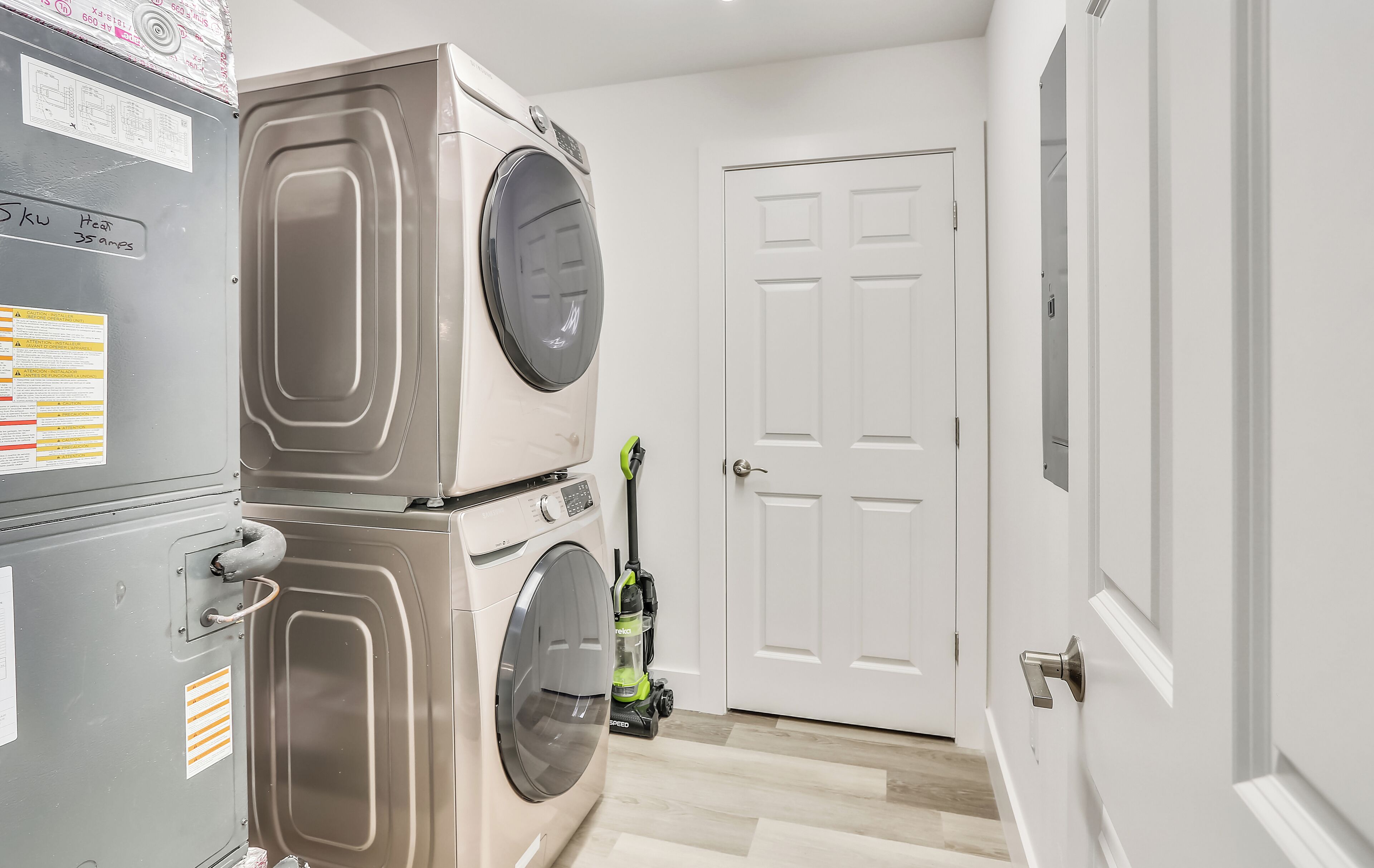 A laundry area with stacked washers and dryers, a vacuum cleaner, and a white door.
