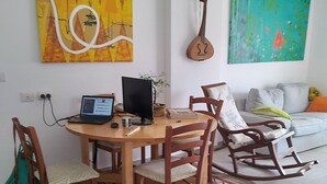 A living room with a wooden dining table, chairs, a laptop, and a guitar hanging on the wall.