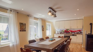A modern kitchen with white cabinets, a dining area with a wooden table, and a view of the outdoors.