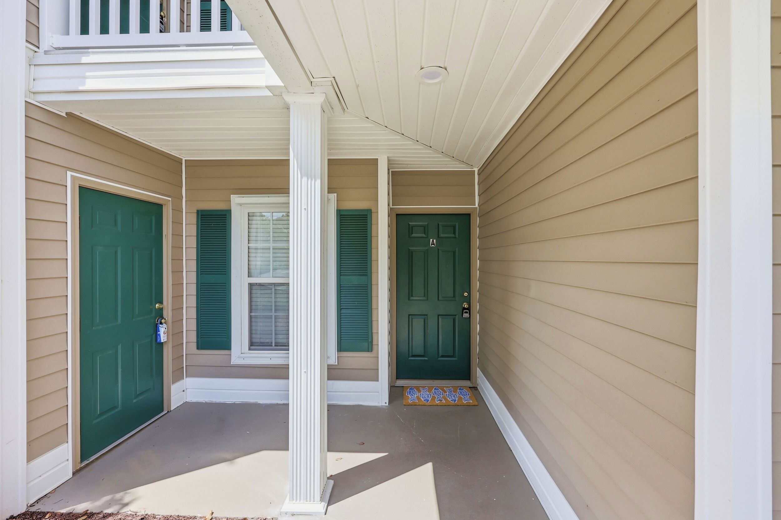 A covered porch with three doors, each with a green door and a window with shutters.