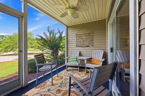 A covered porch with ceiling fans, a small table, and two Adirondack chairs.