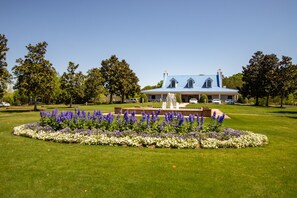 A large house with a blue roof, surrounded by a well-maintained lawn and a circular flower bed with purple and white flowers.