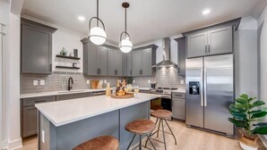 A modern kitchen with grey cabinets, a stainless steel refrigerator, and a central island with stools. - Beautiful Luxury Renovation, 5 minutes to Downtown (Nashville)