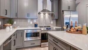 Una cocina moderna con gabinetes grises, electrodomésticos de acero inoxidable y encimera blanca.