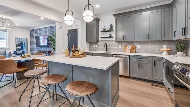 Una cocina moderna con armarios grises, una isla grande con taburetes, iluminación colgante y un horno empotrado.