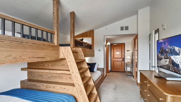 Une chambre d’hôtel moderne avec un escalier en bois, un lit, un bureau et une télévision.