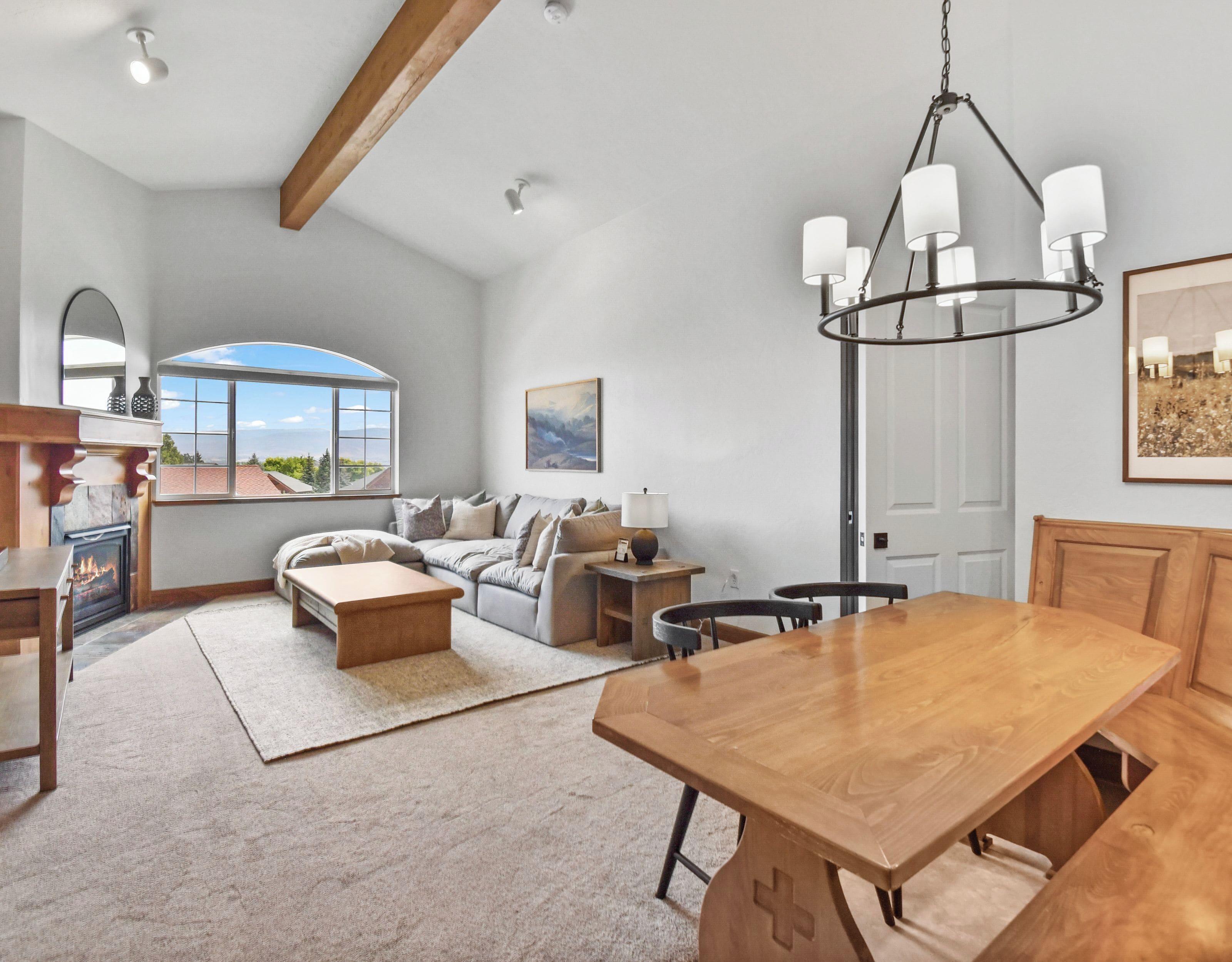 A spacious living room with a fireplace, a wooden dining table, and a large window offering a view of the outdoors.