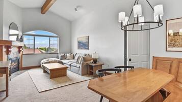A spacious living room with a fireplace, a wooden dining table, and a large window offering a view of the outdoors.