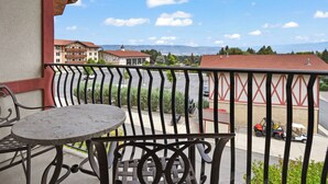Un balcon avec une table et des chaises, donnant sur un parking et des bâtiments aux toits rouges.