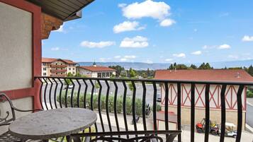 A balcony with a table and chairs, overlooking a parking area and buildings with red roofs.