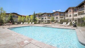 Une piscine entourée de bâtiments à plusieurs étages dotés de balcons, avec des chaises longues et des tables à proximité.