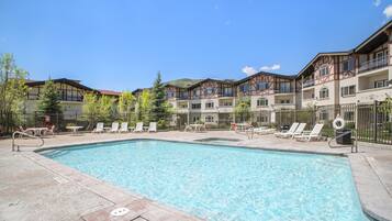 A swimming pool with lounge chairs and tables, surrounded by multi-story buildings with balconies.