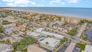 An aerial view of a coastal town with beachfront hotels, a swimming pool, and a clear view of the ocean.