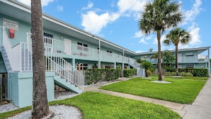 A two-story motel with a light blue exterior, a central staircase, and a well-maintained lawn with palm trees.