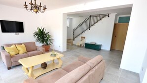 Una sala de estar con sofá, una mesa de centro, televisor, una escalera y una planta en maceta.