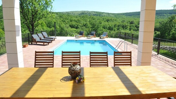 Vista de la piscina con una mesa de madera, cuatro sillas y un jarrón decorativo.