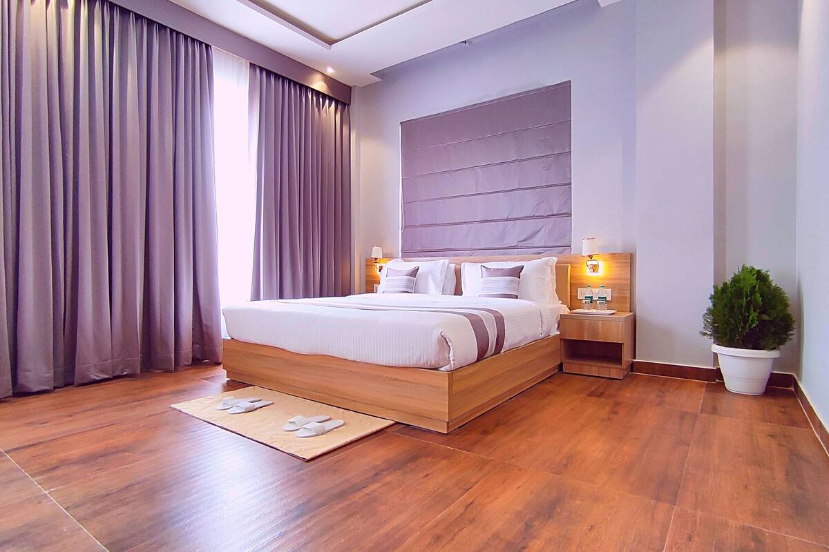 Una camera da letto moderna con un letto di legno, un comodino, una pianta in vaso e un'ampia finestra con tende.