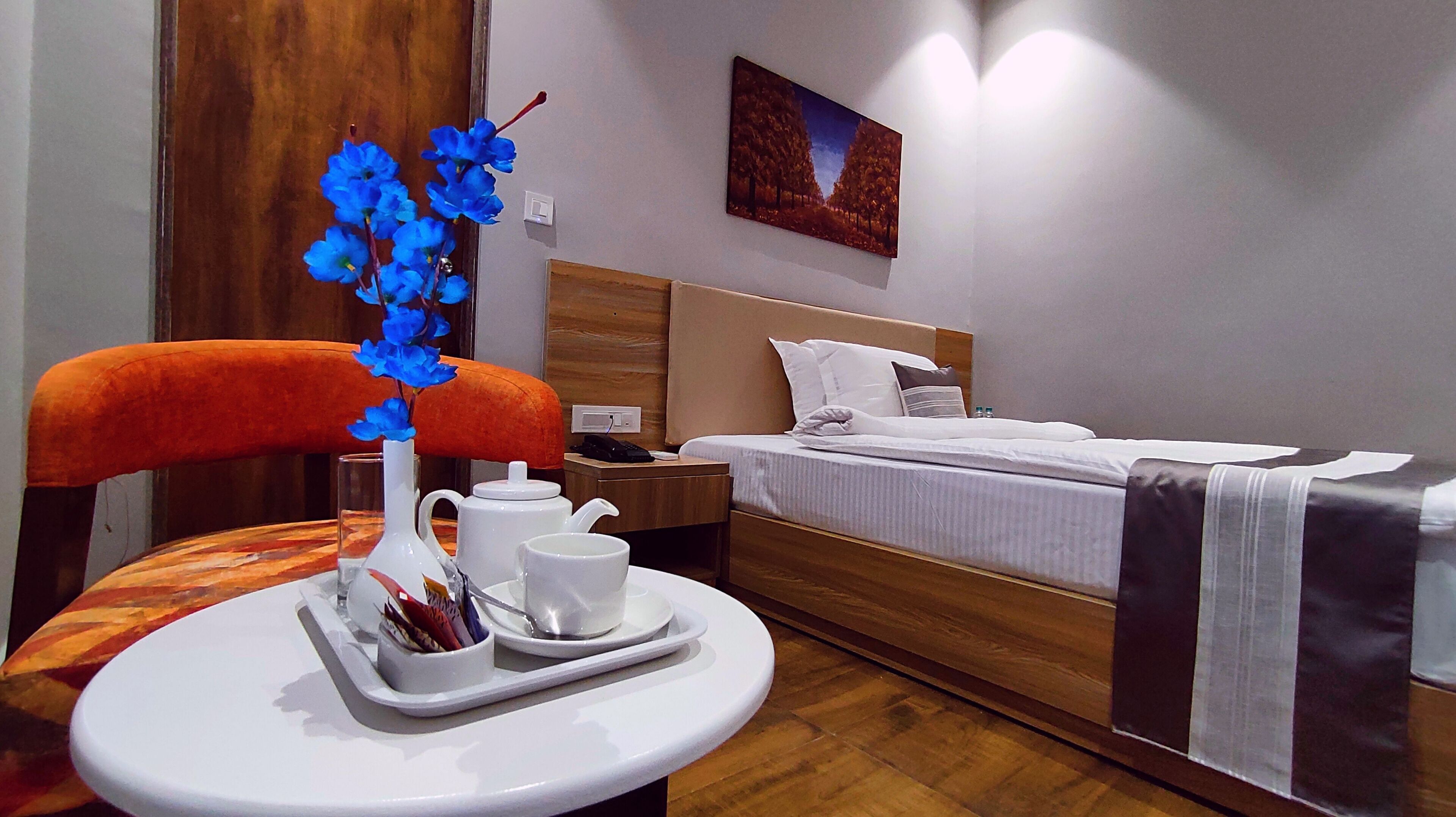 Une chambre d’hôtel avec un lit, une table de chevet, une table sur laquelle se trouve un plateau avec des articles pour le petit-déjeuner, et un tableau accroché au mur.