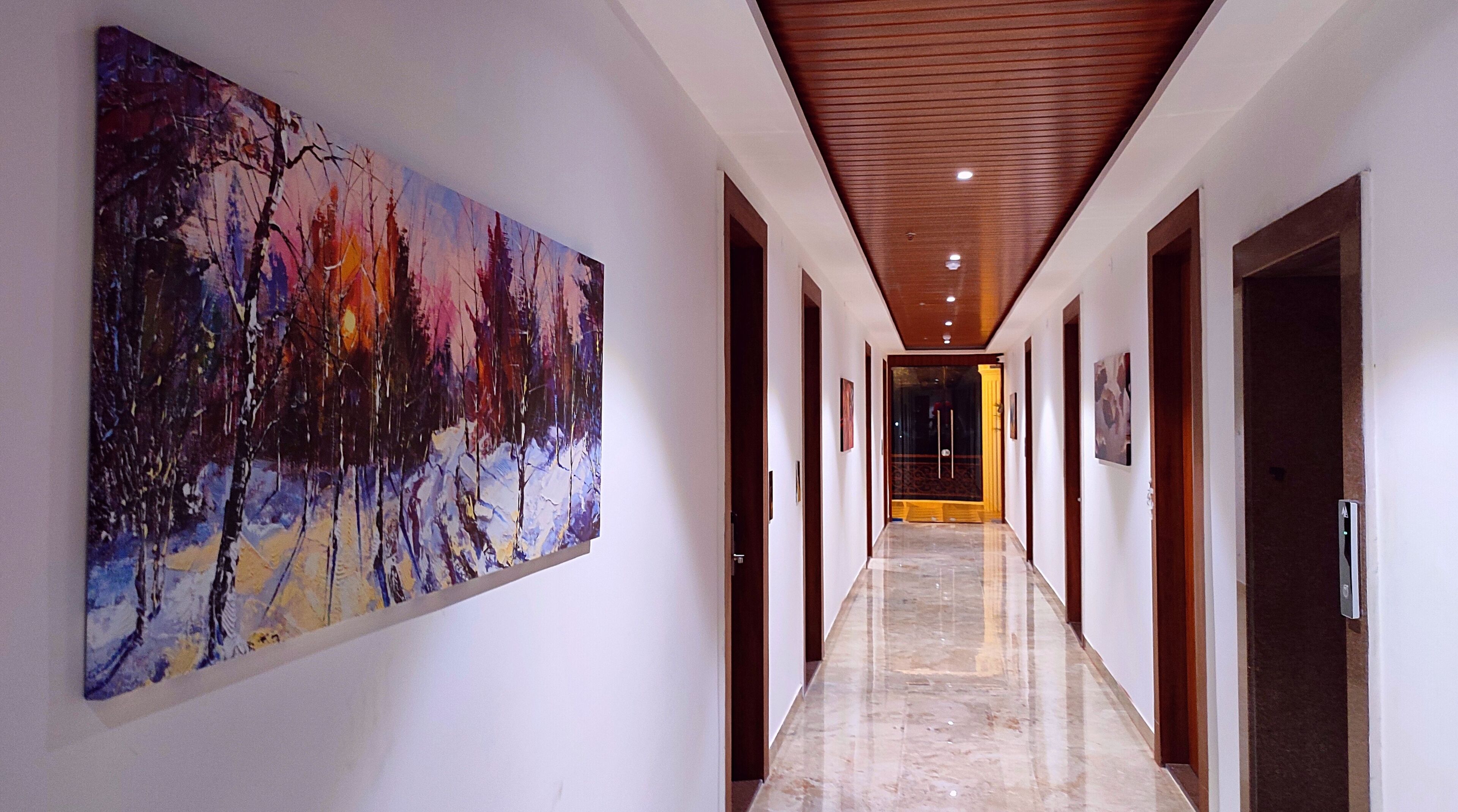 A hallway with a large abstract painting on the left wall, wooden doors on the right, and a marble floor.