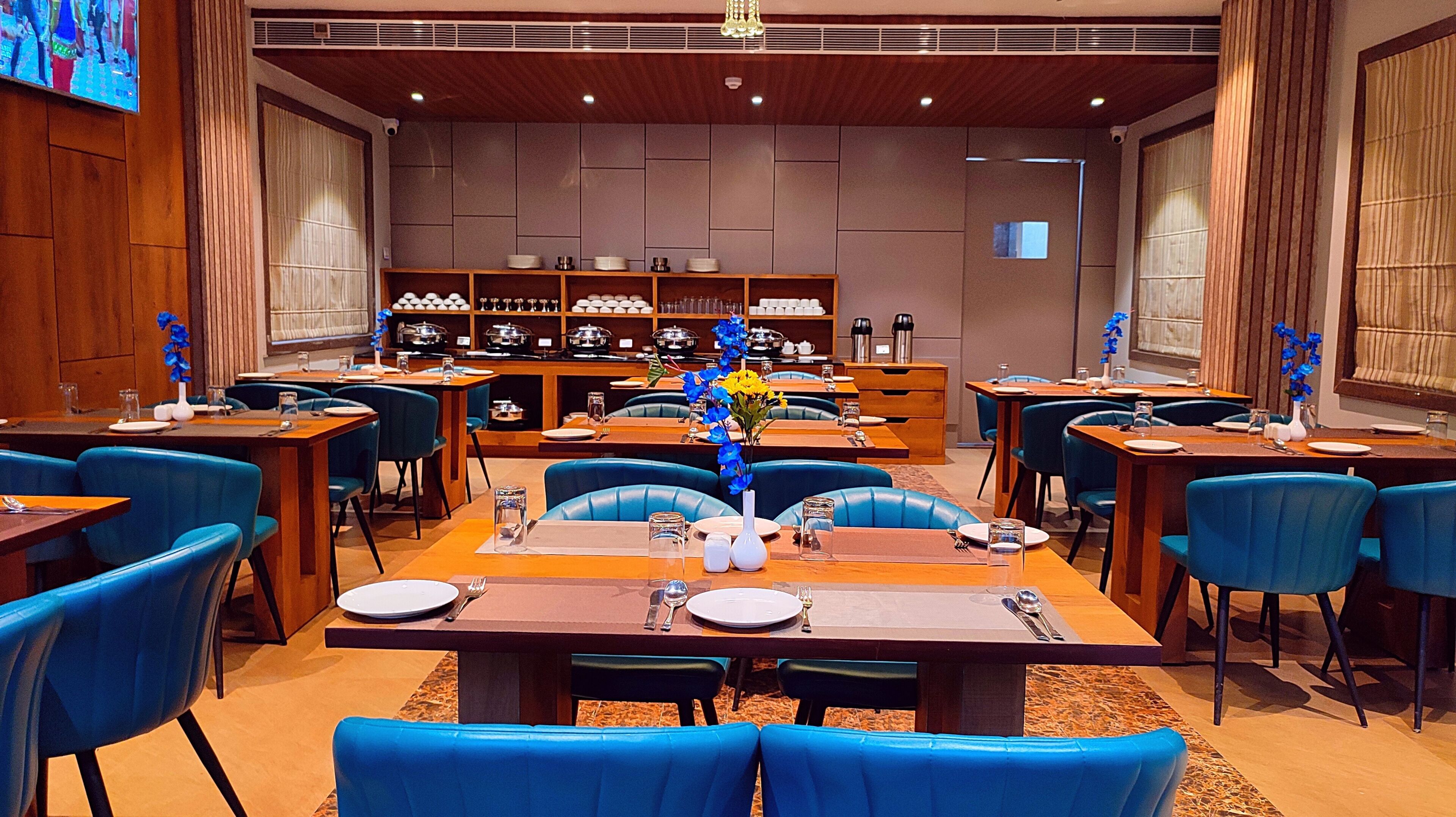 A restaurant with blue chairs, wooden tables, and a buffet area in the background.
