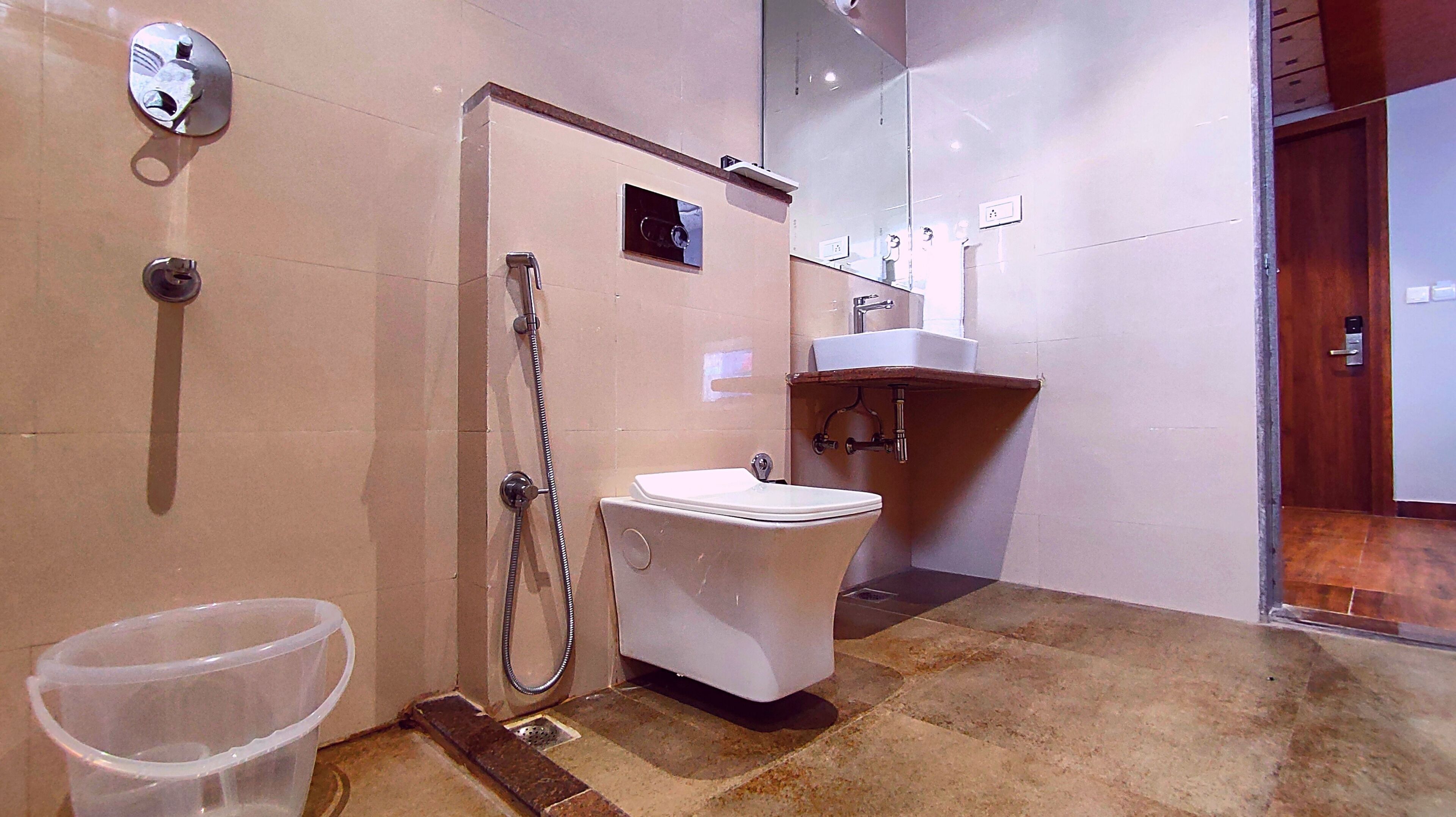 A bathroom with a toilet, a shower, a sink, and a trash bin.