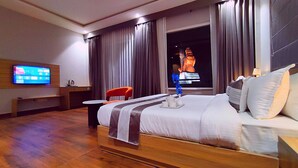 Habitación de hotel con cama, escritorio, silla, televisor y ventana con cortinas.