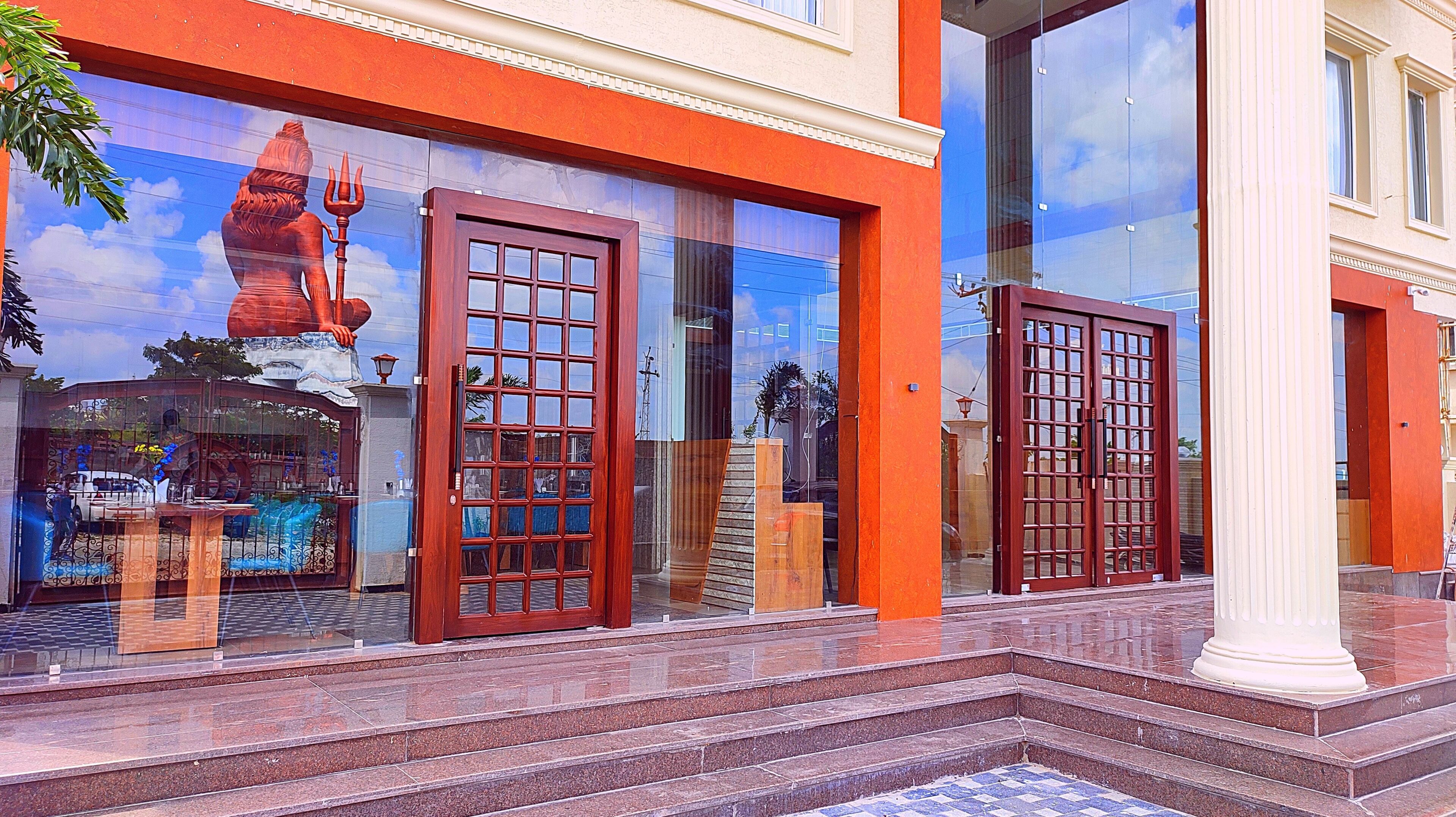 A building with large glass windows, a red door, and a staircase leading to the entrance.