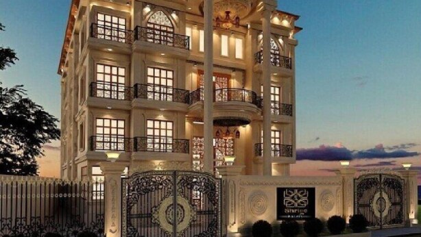 Un edificio de varios pisos con balcones, ventanas grandes y un portón decorativo.