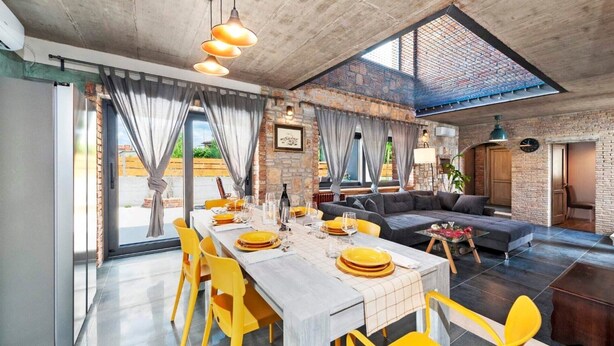 A spacious dining area with a long table set for a meal, a cozy living area with a sofa, and a view of the outdoors through large windows. - Modern Villa Baraka with a pool (Kanfanar)