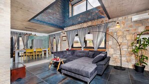 A spacious living area with a stone wall, a large gray sofa, a dining table with chairs, and a ceiling with a blue net-like structure. - Modern Villa Baraka with a pool (Kanfanar)