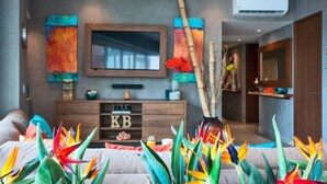 A modern living room with a large flat-screen TV, a wooden console table with decorative items, and vibrant tropical plants. - Casa Paraiso - Luxury 2 Bed 3 Bath at Pavilion Lux (Puerto Vallarta)