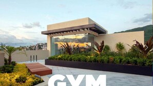 A modern building with a glass facade, surrounded by landscaped gardens and a view of a bridge. - Casa Paraiso - Luxury 2 Bed 3 Bath at Pavilion Lux (Puerto Vallarta)