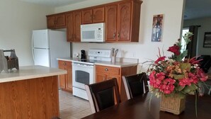 A kitchen with wooden cabinets, a white refrigerator, a microwave, an oven, and a dining table with chairs. - Spacious 3BR 2BA, 11 Min to Cummins Falls Park (Cookeville)
